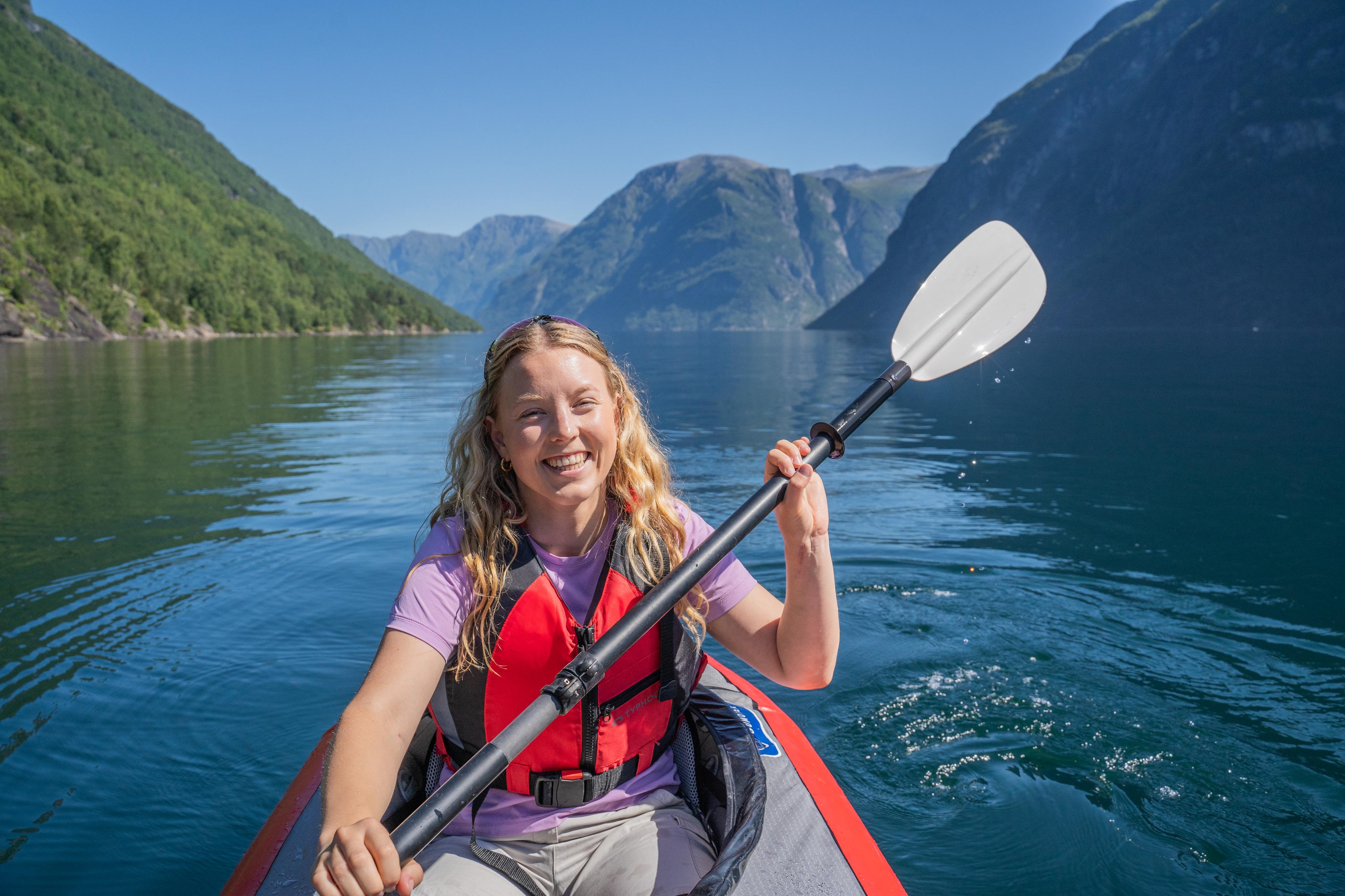 Kayaker smiling in a fjord with dramatic mountains behind